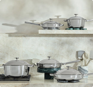 Set of titanium cookware on a kitchen counter with a marble backsplash.