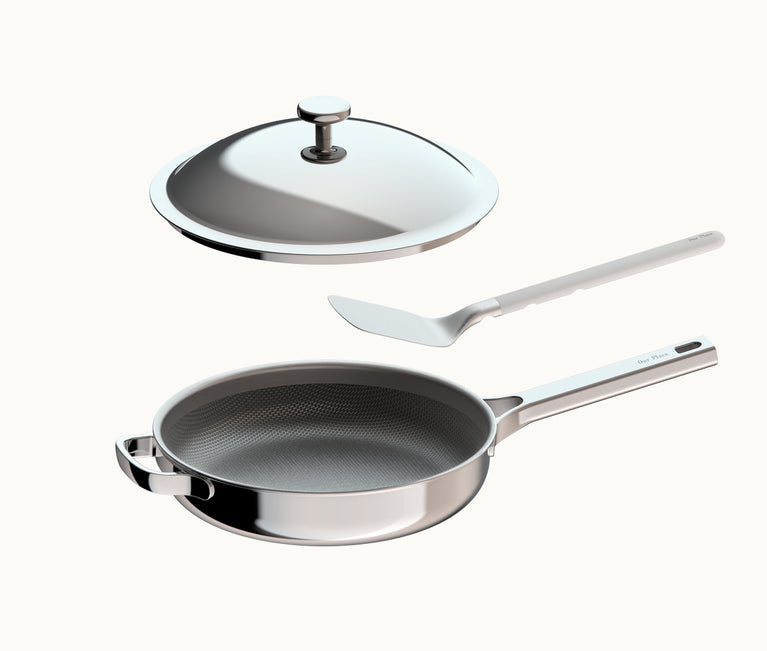 A stainless steel frying pan with a textured interior, a matching lid, and a metal spatula.