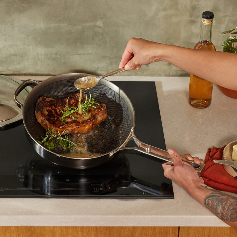 A chef cooks a steak in a chrome Titanium Always Pan Pro on the stove