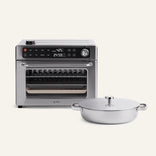 The Wonder Oven® Pro + Braiser Set, featuring a stainless steel countertop oven with digital controls and a round, lidded titanium braiser pan with handles, is set against a plain light background.