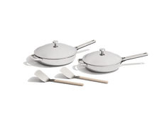 Two stainless steel frying pans with lids and two white spatulas are arranged on a plain white background.