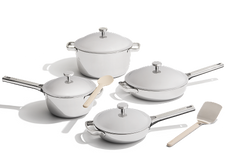 A set of four stainless steel cookware pieces with lids, accompanied by a wooden spoon and spatula, arranged on a white background.