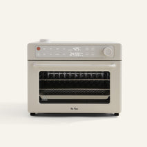 A beige countertop oven with digital display, control knobs, and a glass door showing racks and a pan inside.