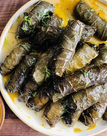 A plate of stuffed grape leaves arranged closely together, garnished with herbs and drizzled with oil.