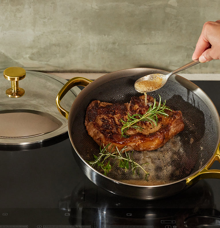 Person cooking pork chops with herbs in a frying pan on a stove.