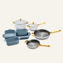 The Titanium Pro Cookware + Bakeware Set (2.0) features high-performance stainless steel cookware with gold-toned handles and lids alongside several matte blue ceramic bakeware dishes.