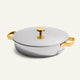 A round silver Titanium Braiser Pro 28 cm stainless steel casserole dish with a lid, featuring chef-approved gold-colored handles and a matching gold knob on top, is placed on a plain off-white background.