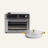 The Wonder Oven® Pro + Braiser Set is displayed on a white surface, with the stainless steel, digitally controlled Wonder Oven® Pro positioned behind the round silver titanium braiser pan, which features a gold handle and lid.