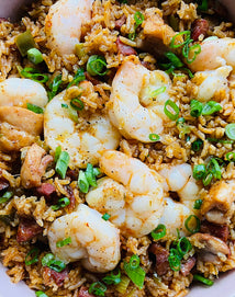 A close-up of shrimp, rice, sausage, chicken, and chopped green onions mixed together in a flavorful Cajun-style dish.