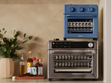 Blue and silver toaster oven on a kitchen counter with bottles and a plant.