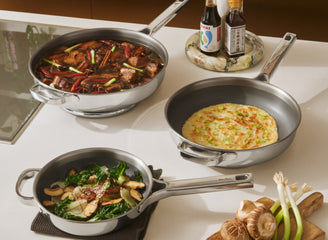 Three frying pans with different dishes on a kitchen counter, accompanied by condiments and ingredients.