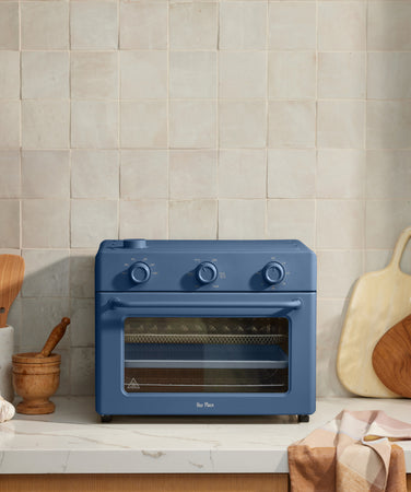 blue large wonder oven on counter surrounded by an assortment of cooked food