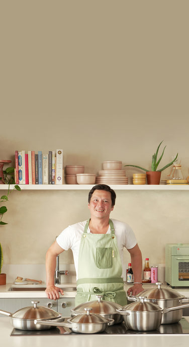 Person in a kitchen holding a silver pan with various pans on a stove.