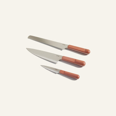 Three kitchen knives with silver blades and brown handles are arranged on a plain light background. The set includes a bread knife, a chefs knife, and a paring knife.