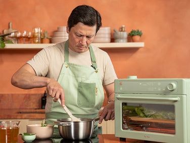 Man in a kitchen stirring a pot with an oven in the background