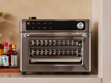 Modern toaster oven on a kitchen counter with various bottles in the background