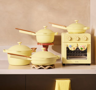 Set of yellow cookware including pots and a small stove on a beige surface.