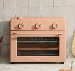 Pink oven with three knobs on a tiled wall background