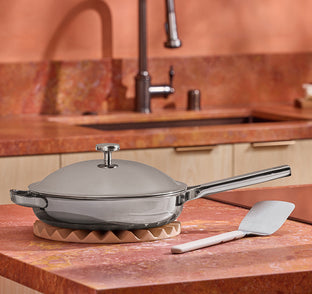 Silver frying pan with a wooden base on a kitchen counter