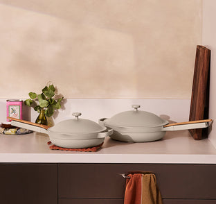 Two beige ceramic pots with wooden handles on a kitchen counter.