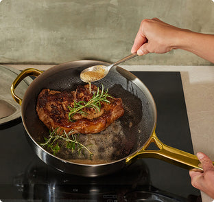 Person seasoning a pan of meat with herbs on a stove.