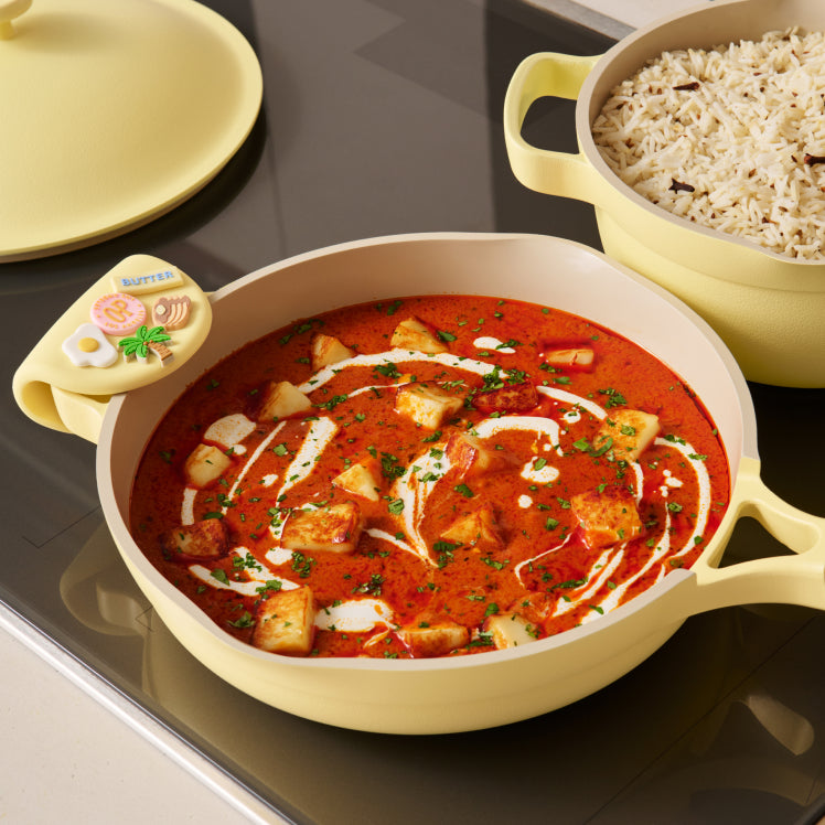 Yellow ceramic dish with a red curry dish and a side of rice on a stove.