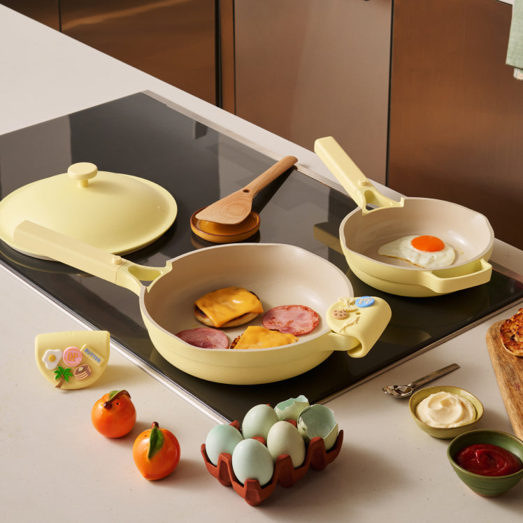 Set of yellow cookware on a stove with food items and condiments.