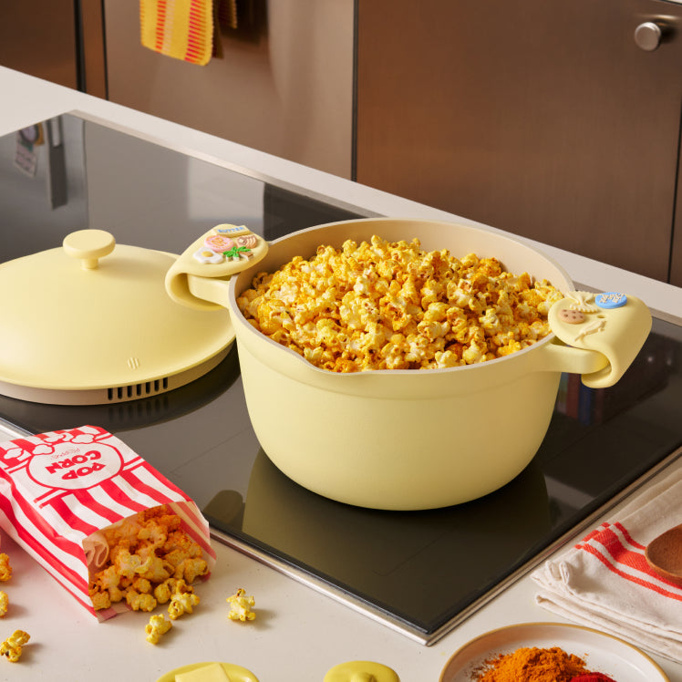 Yellow pot filled with popcorn on a kitchen counter with a microwave and popcorn bags in the background.