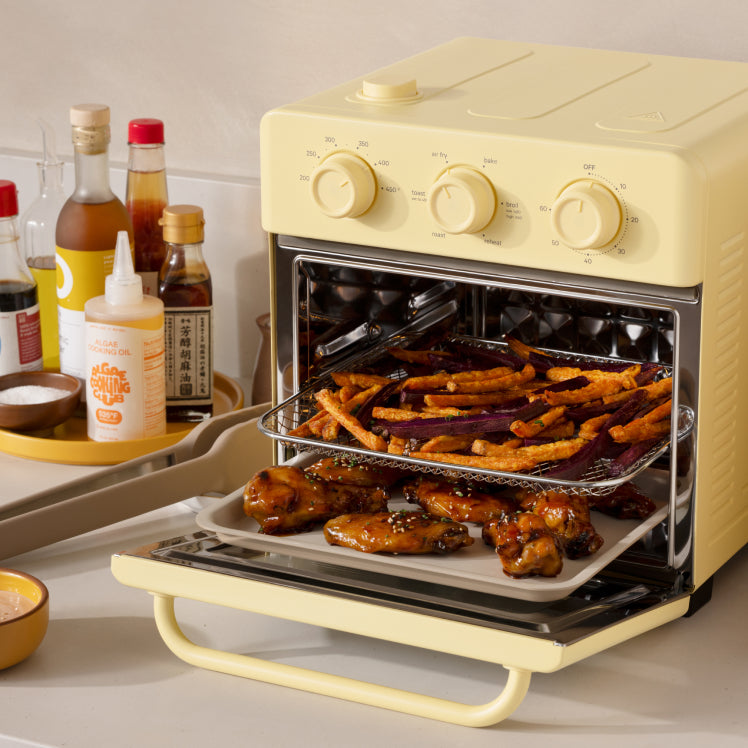 Yellow toaster oven with food inside on a kitchen counter, surrounded by condiments.