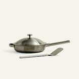 Stainless steel frying pan with lid and spatula on a white background