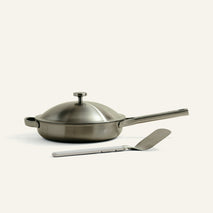 Stainless steel frying pan with lid and spatula on a white background