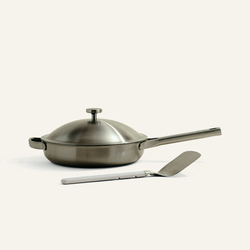 Stainless steel frying pan with lid and spatula on a white background