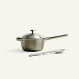 Stainless steel saucepan with lid and spatula on a white background