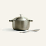 Stainless steel pot with lid and spoon on a light beige background