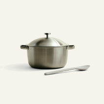 Stainless steel pot with lid and spoon on a light beige background