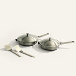 Set of stainless steel cookware with lids and spatulas on a light background