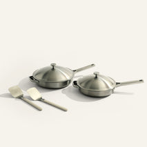 Set of stainless steel cookware with lids and spatulas on a light background