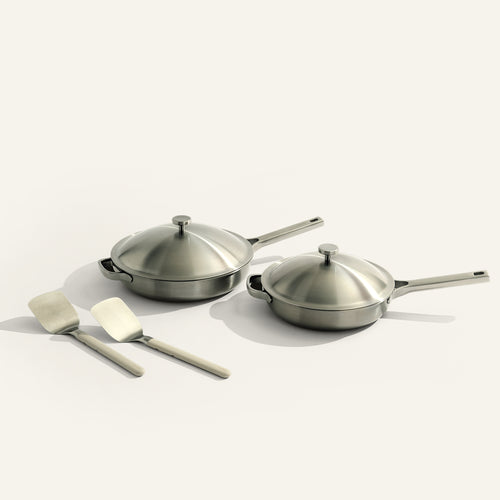 Set of stainless steel cookware with lids and spatulas on a light background