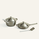 Set of stainless steel cookware including a pot, pan, and spatula on a white background