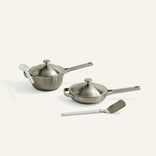 Set of stainless steel cookware with lids and a spatula on a white background