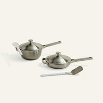 Set of stainless steel cookware with lids and a spatula on a white background