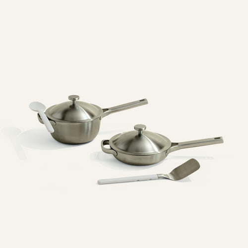 Set of stainless steel cookware with lids and a spatula on a white background