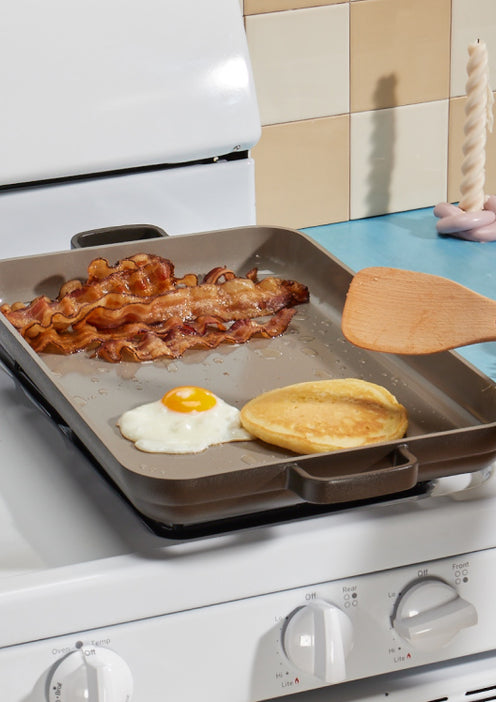 black griddle pan on stove cooking bacon, eggs and pancakes