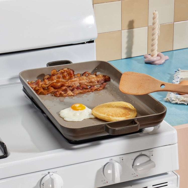 black griddle pan on stove cooking bacon, eggs and pancakes