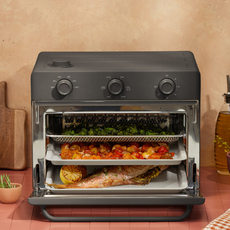 cooking vegetables, and fish on three trays in black large wonder oven on counter