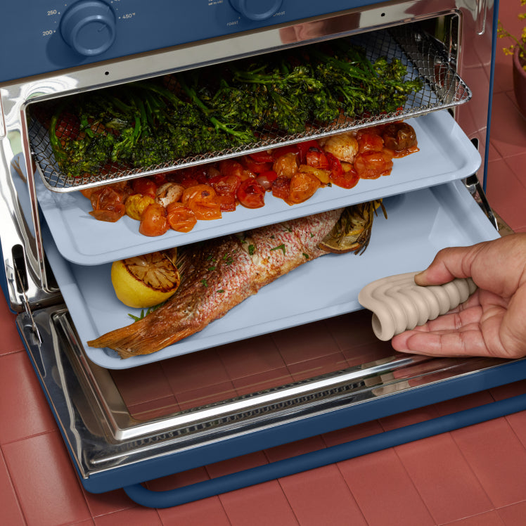 cooking vegetables, and fish on three trays in blue large wonder oven on counter