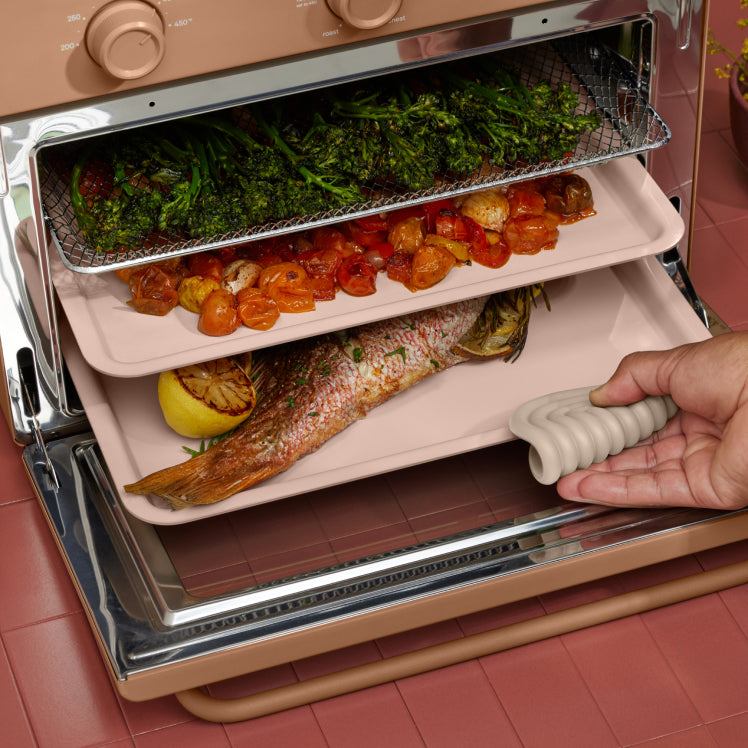 cooking vegetables, and fish on three trays in pink large wonder oven on counter