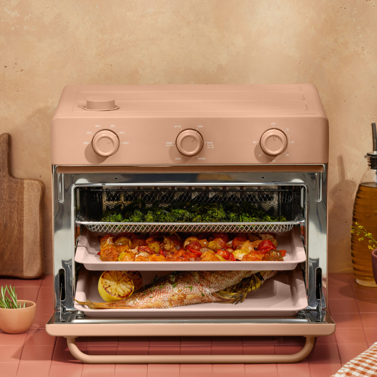 cooking vegetables, and fish on three trays in pink large wonder oven on counter