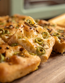 Close-up of a pizza with green olives and rosemary on a wooden surface