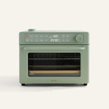A sage green countertop oven with digital display showing 425°F and 24:59, a control knob, buttons, and a glass door revealing cooking racks inside.